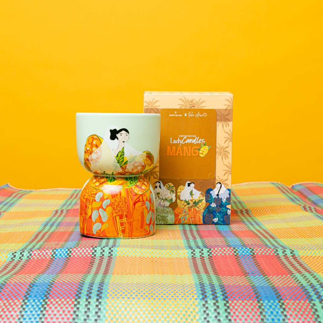 Decorative candle including a box, and small figurine on a colorful checkered tablecloth with a yellow background.