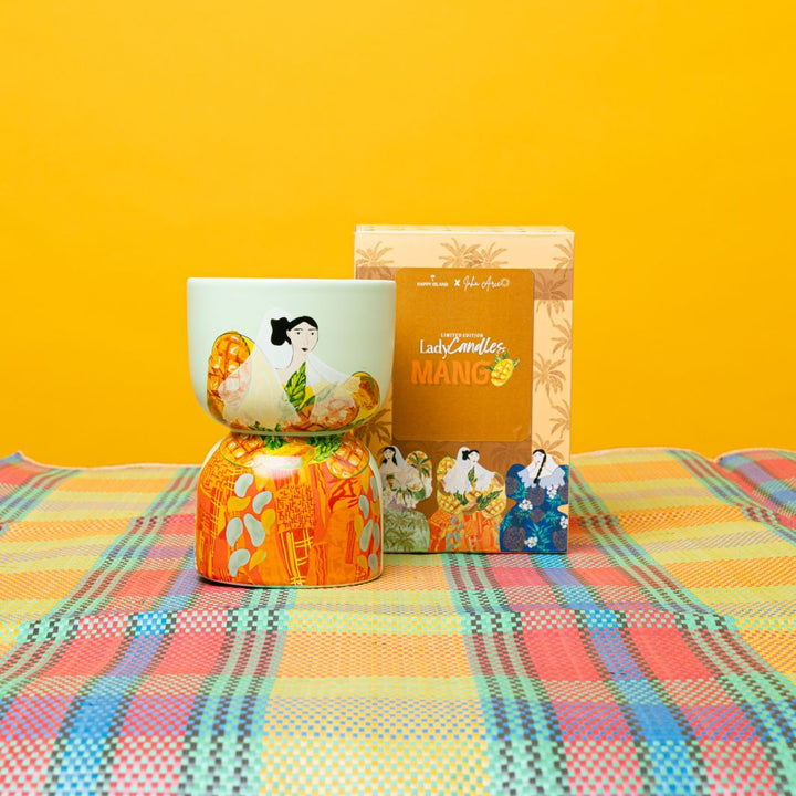 Decorative candle including a box, and small figurine on a colorful checkered tablecloth with a yellow background.